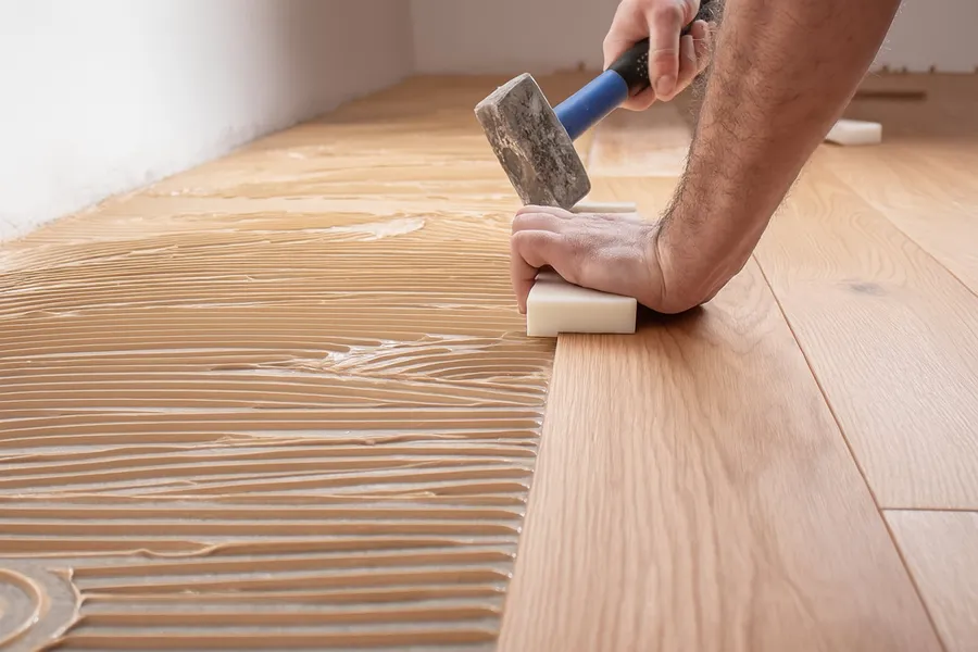 Handwerker verlegt Holzboden mit einem Gummihammer