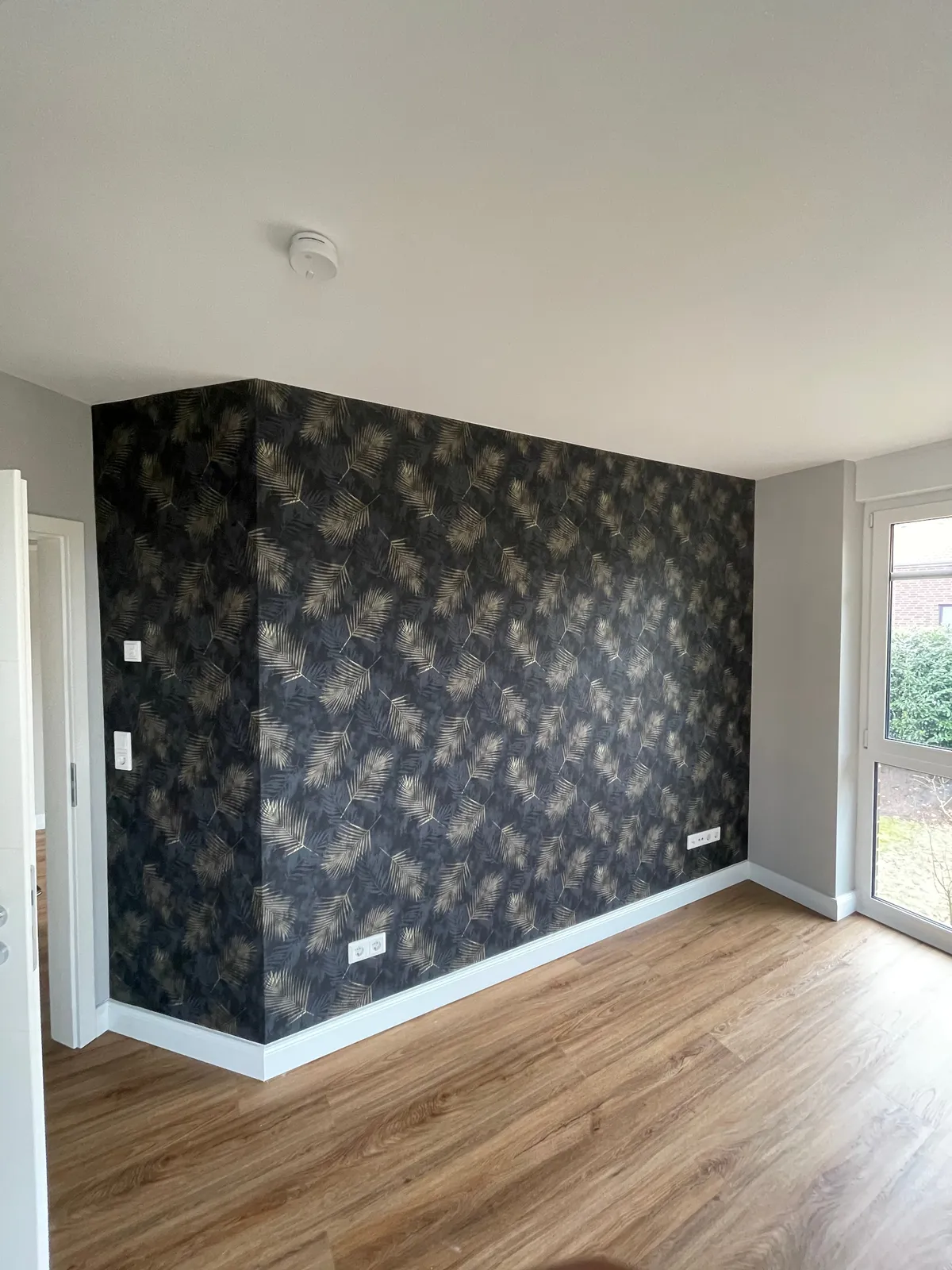 Zimmer mit dunkler Mustertapete an der Wand und hellem Holzboden
